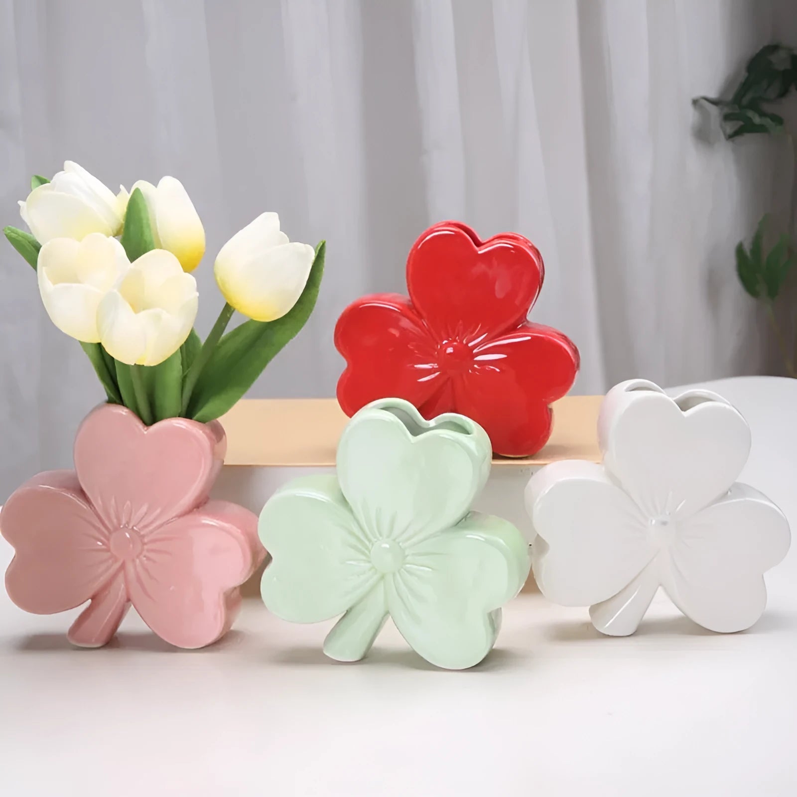 European style white porcelain ceramic vase in four colour options on a desktop.
