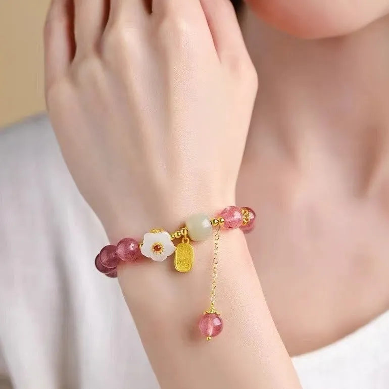 Handmade strawberry quartz crystal bracelet with peach blossom design on a wrist.
