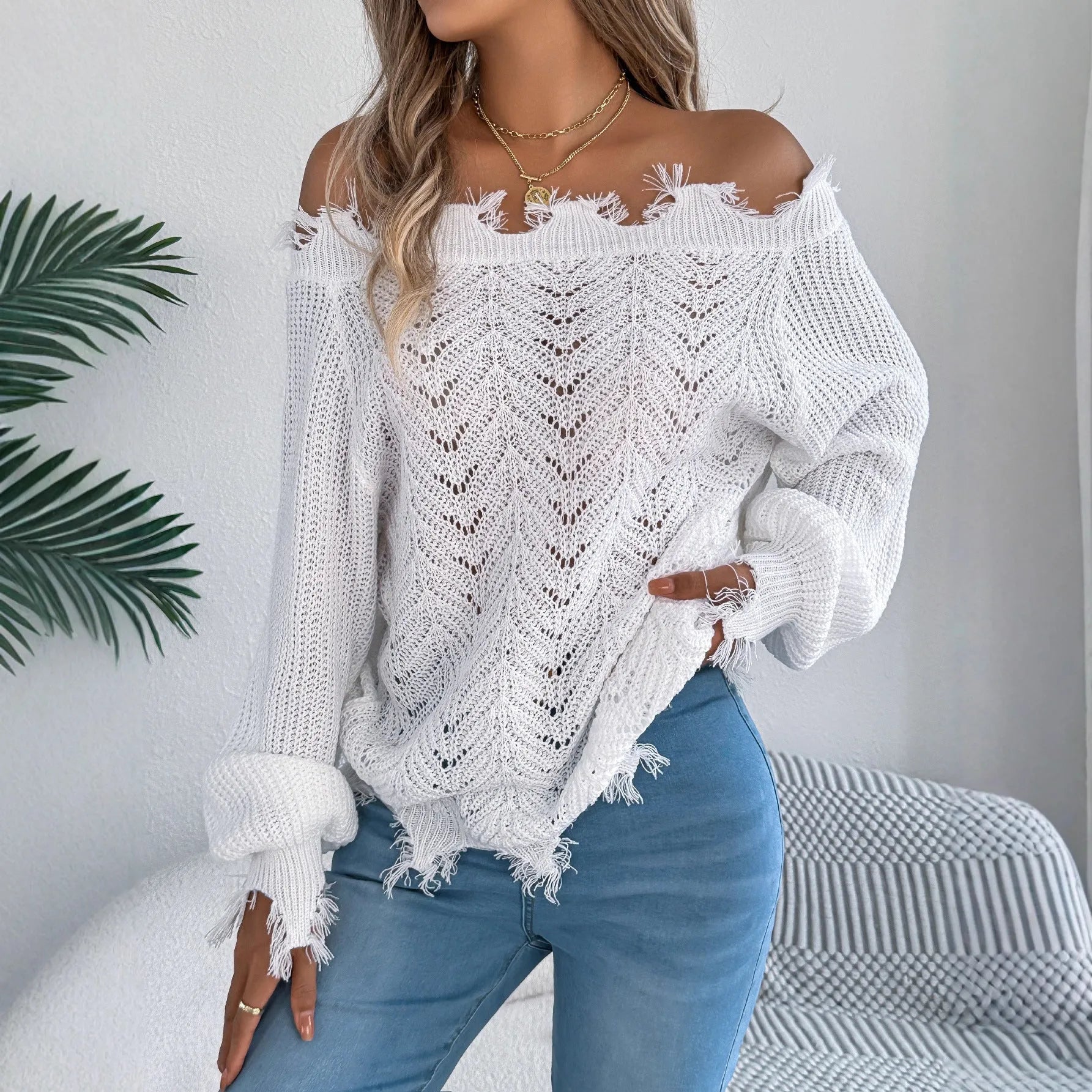 White hollow-out long sleeve pullover sweater with an off-the-shoulder neckline on a hanger.