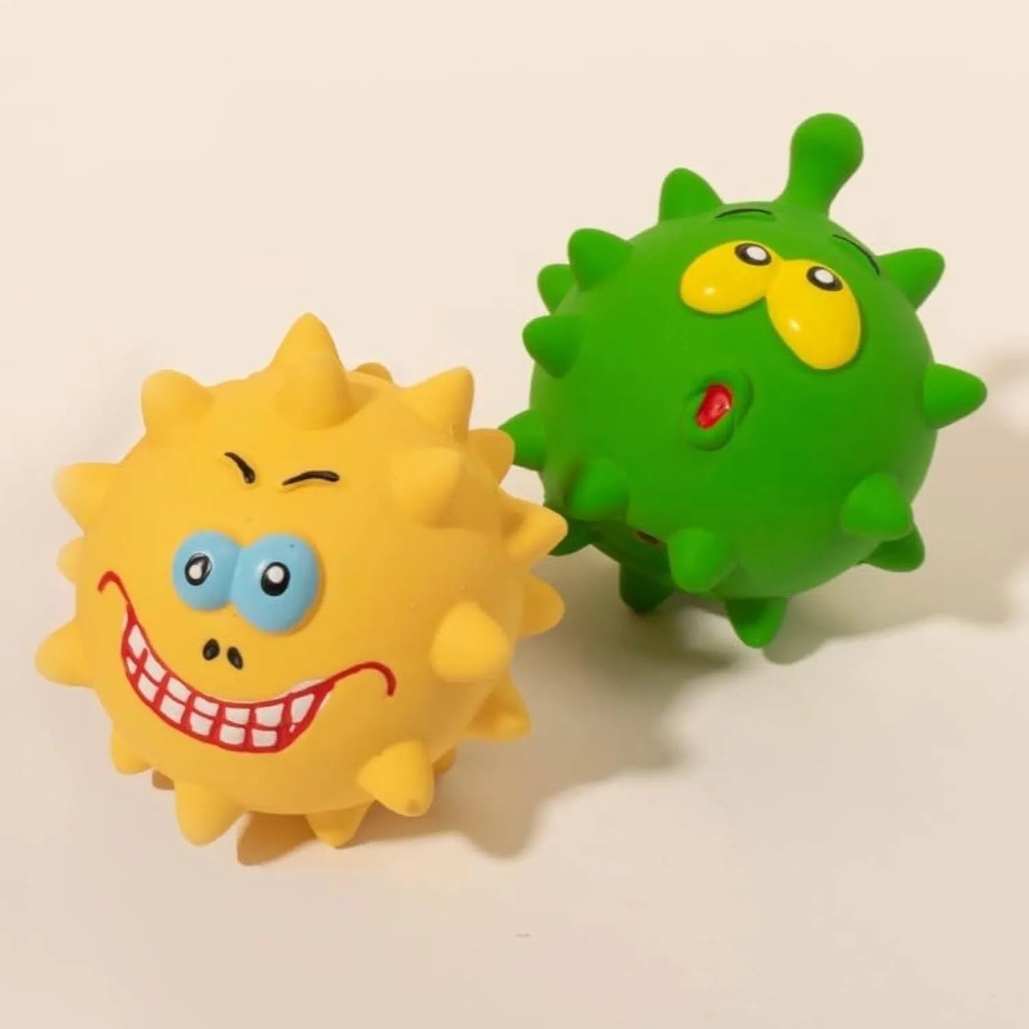 Set of four coloured squeaky dog balls with cute faces on a bumpy latex rubber surface.