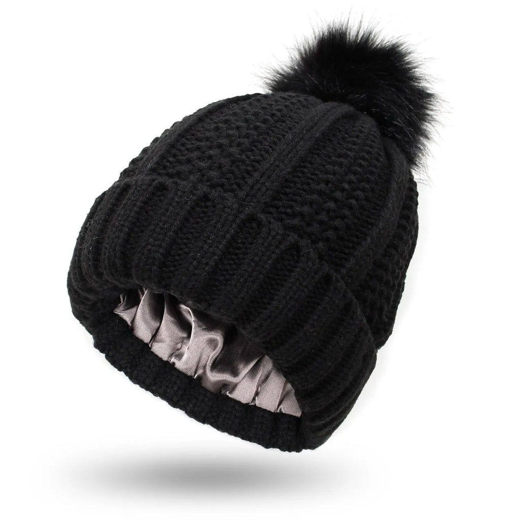 Women's knitted beanie hat with satin lining and a faux fur pom pom in a choice of eight colours.