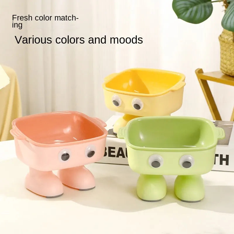 Green cartoon robot-shaped elevated cat bowl with tilted design and non-slip base on a table.