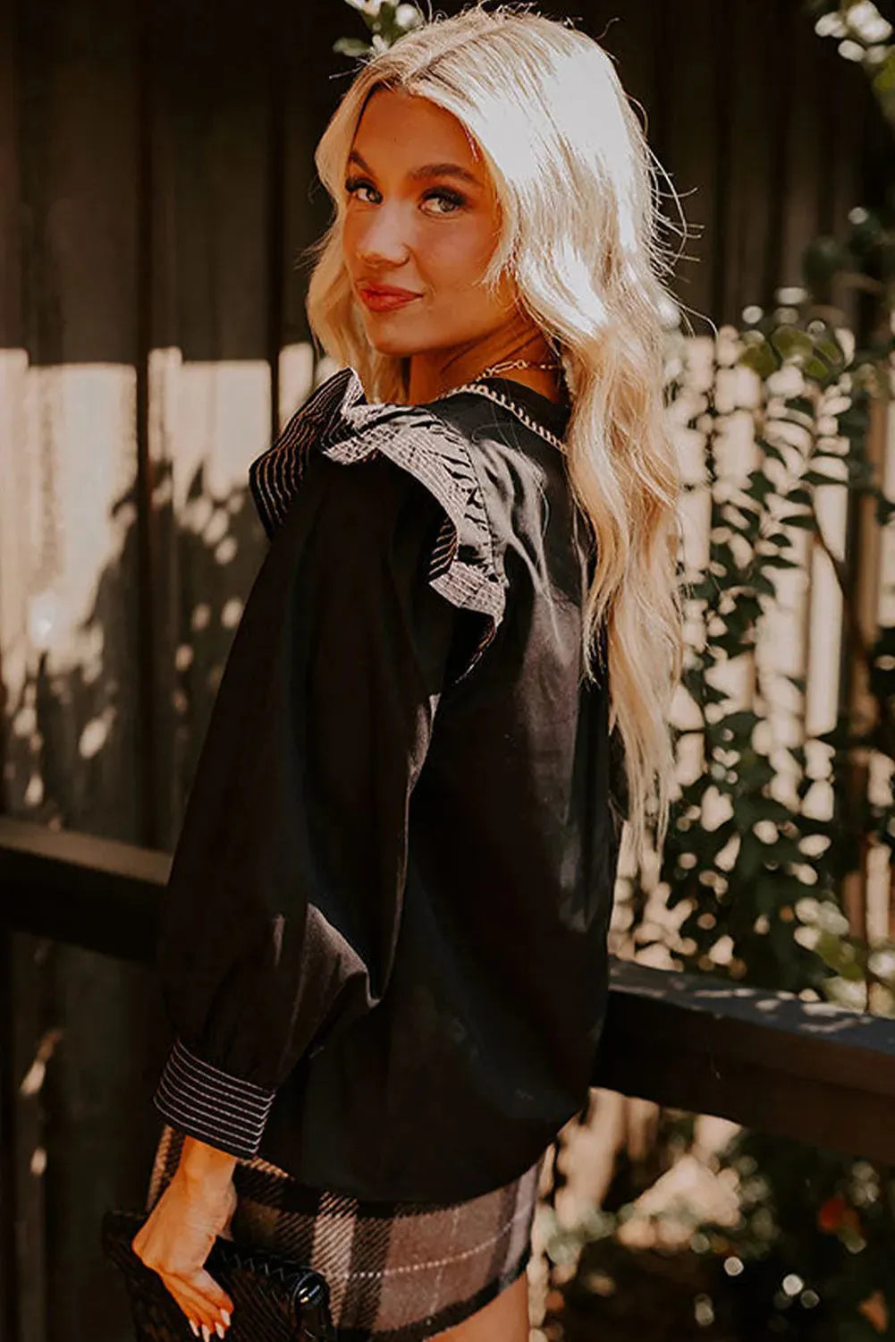 Black long sleeve V-neck blouse with contrast stitching and three-quarter ruffle sleeves.