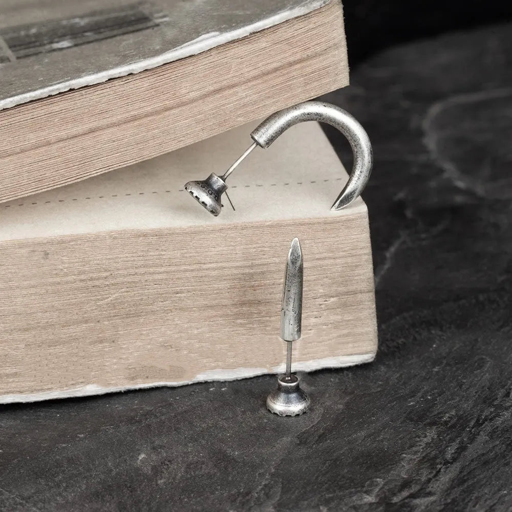 Close-up of a sterling silver punk stud earring with a retro nail design on an ear.
