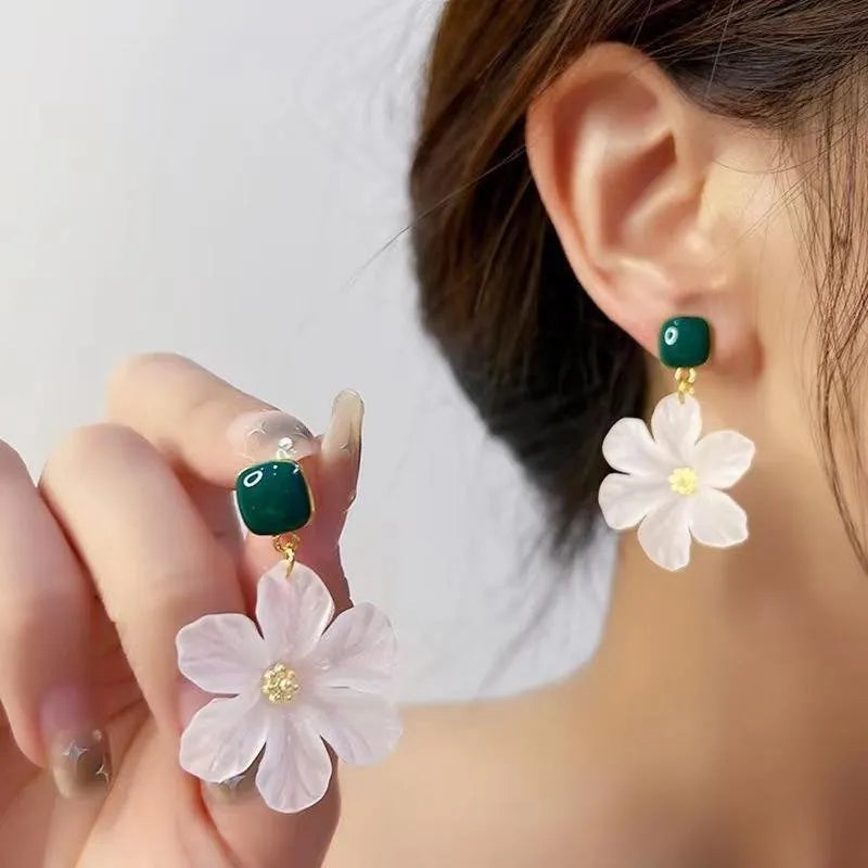A pair of dark green alloy drop earrings with a floral design and clip-on fittings.