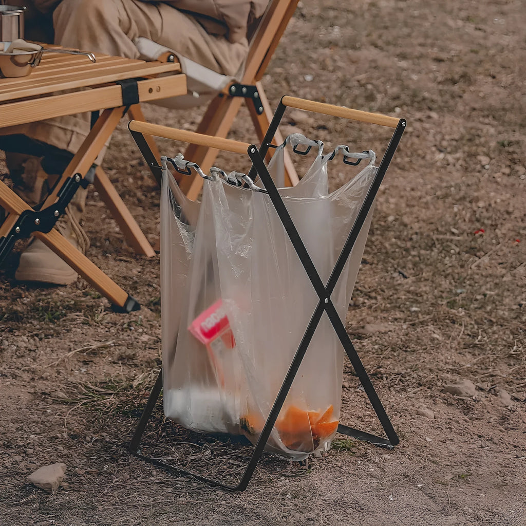 Black folding iron trash storage rack with a wooden handle holding a bin bag.