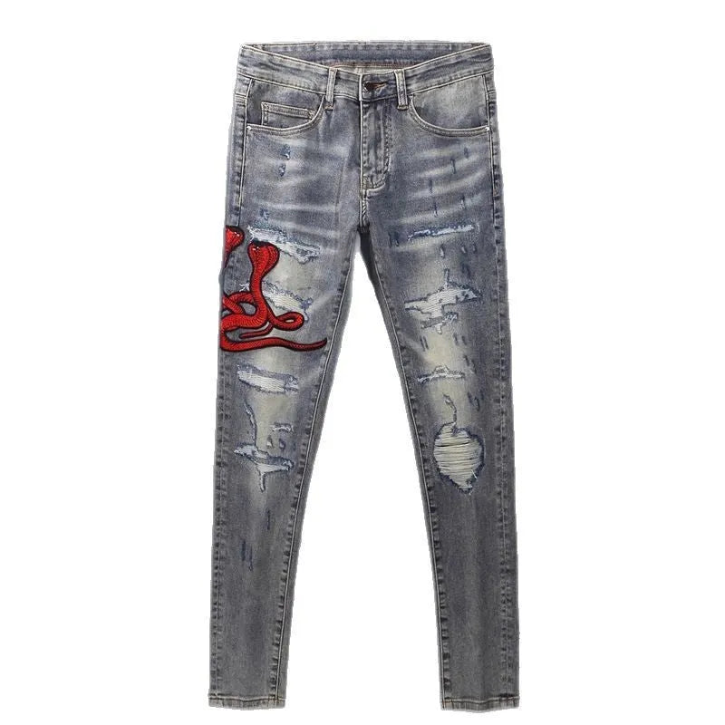Man wearing slim fit distressed blue jeans with hole patches and embroidered details on the legs.