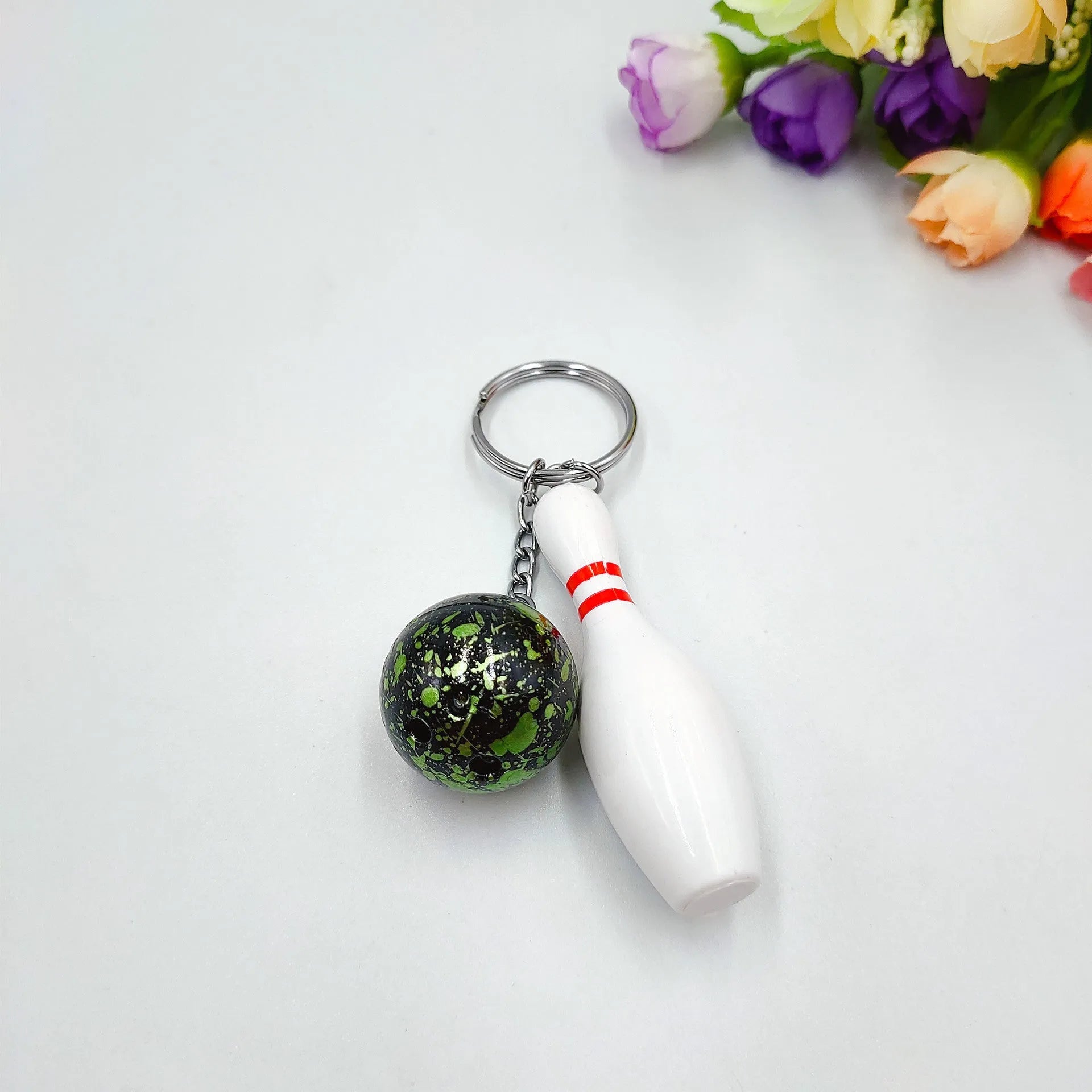 Miniature dark red bowling ball keychain on a metal ring with blue, purple, and green colour options shown