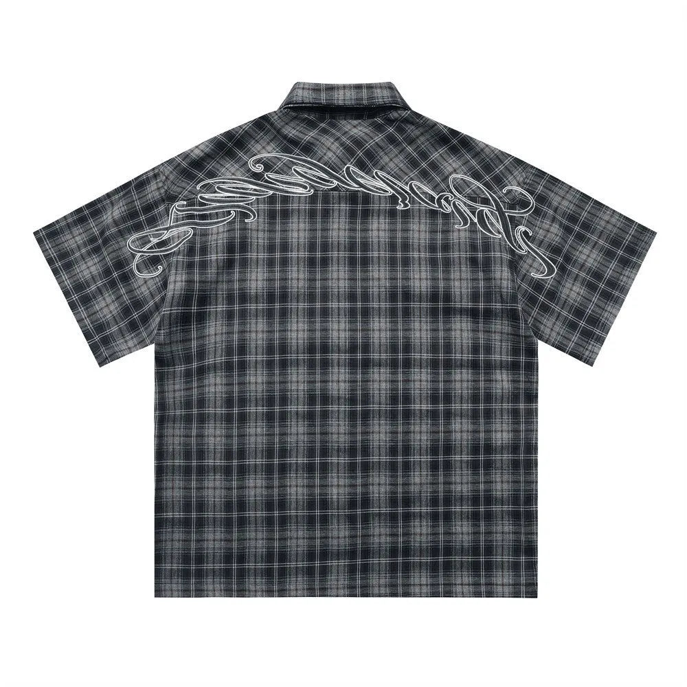 Man wearing a black loose-fit plaid short sleeve shirt with embroidered lettering on the chest.