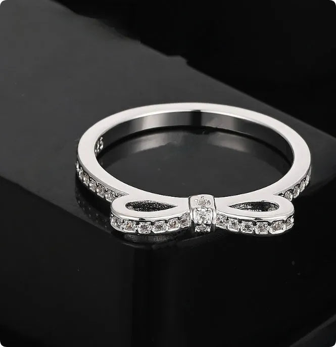 Silver couple ring with a bow-shaped centre decorated with sparkling rhinestone crystals on a finger.