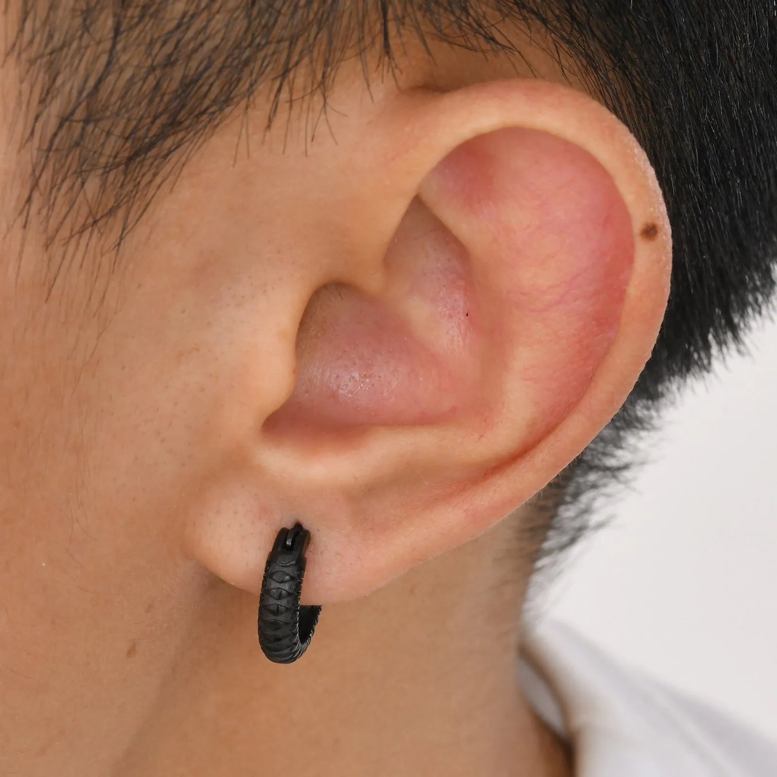 Close-up of a black stainless steel earring with a detailed snake pattern and hook fastening.