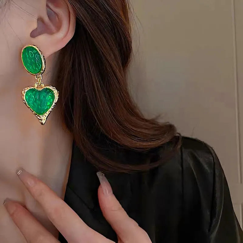 Close-up of a pair of textured needle-pleated oval heart stud earrings in an alloy metal, showing colour options.