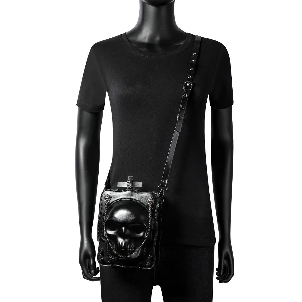 Black square crossbody bag with embossed skull design, chain accents, and zip opening