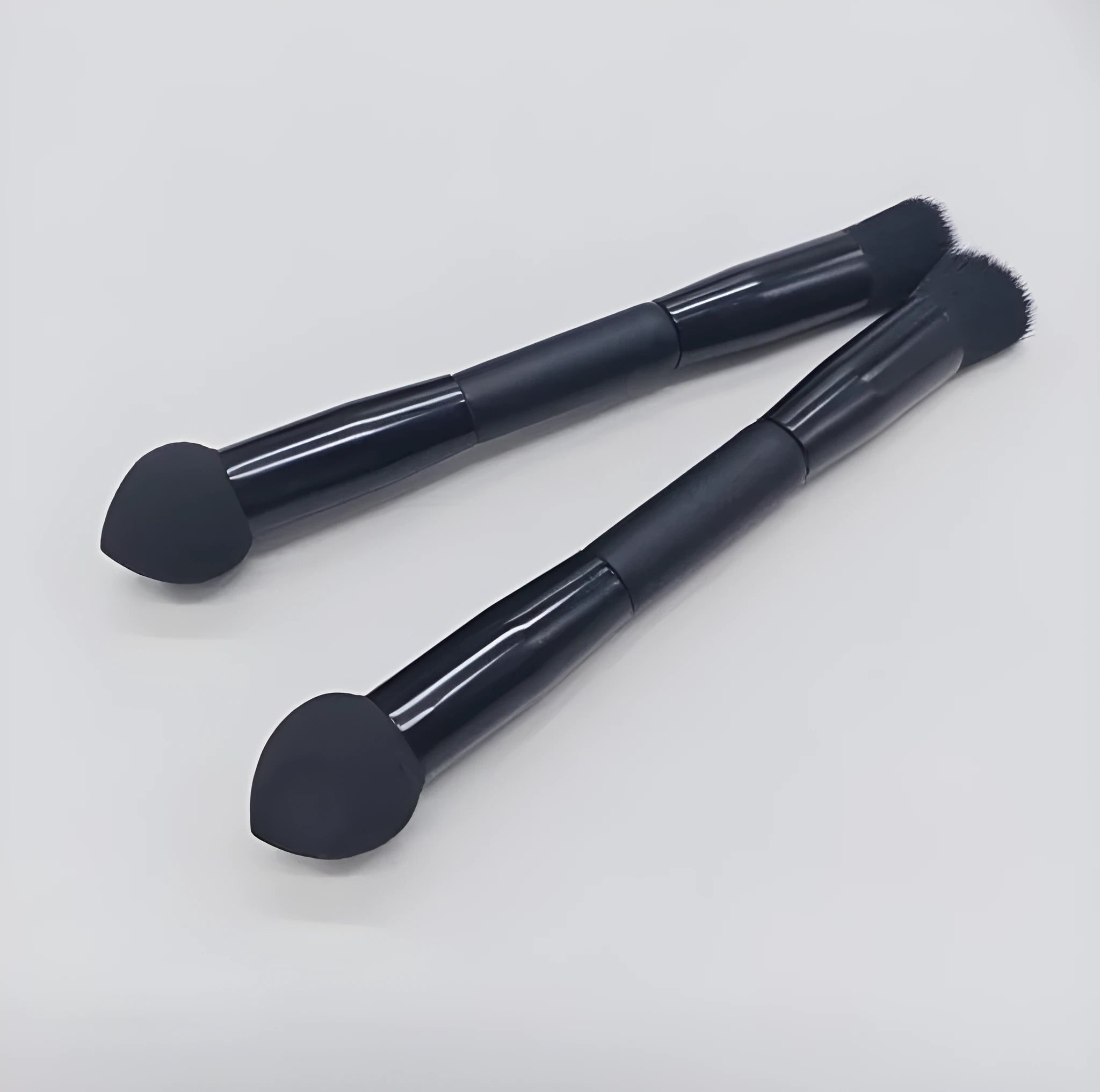 Double-headed concealer brush with tapered bristles and a miter sponge on a long black wooden handle.