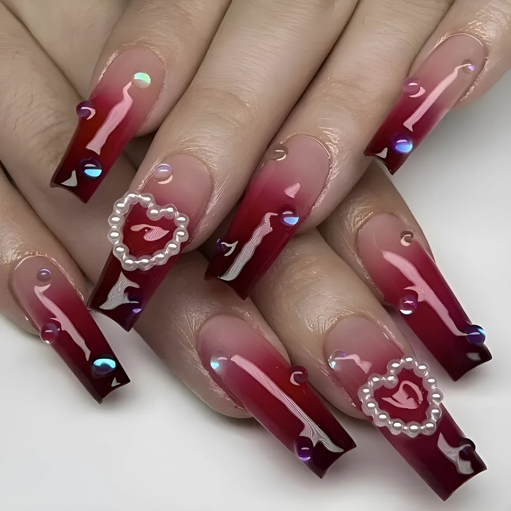 Set of long wine red gradient fake nail tips with pearl and heart design on a plaid pattern, shown with jelly glue and rubbing clause.