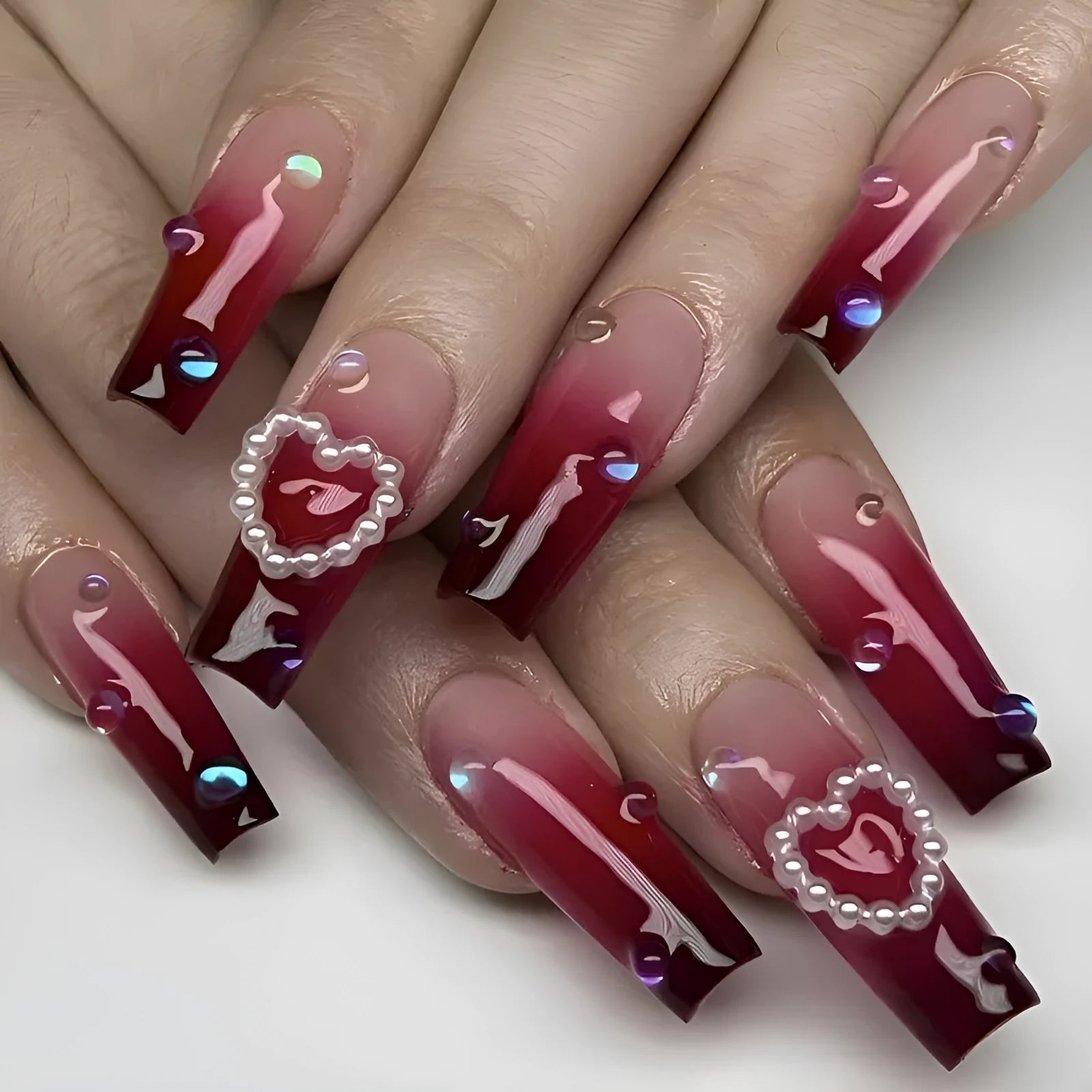 Set of long wine red gradient fake nail tips with pearl and heart design on a plaid pattern, shown with jelly glue and rubbing clause.