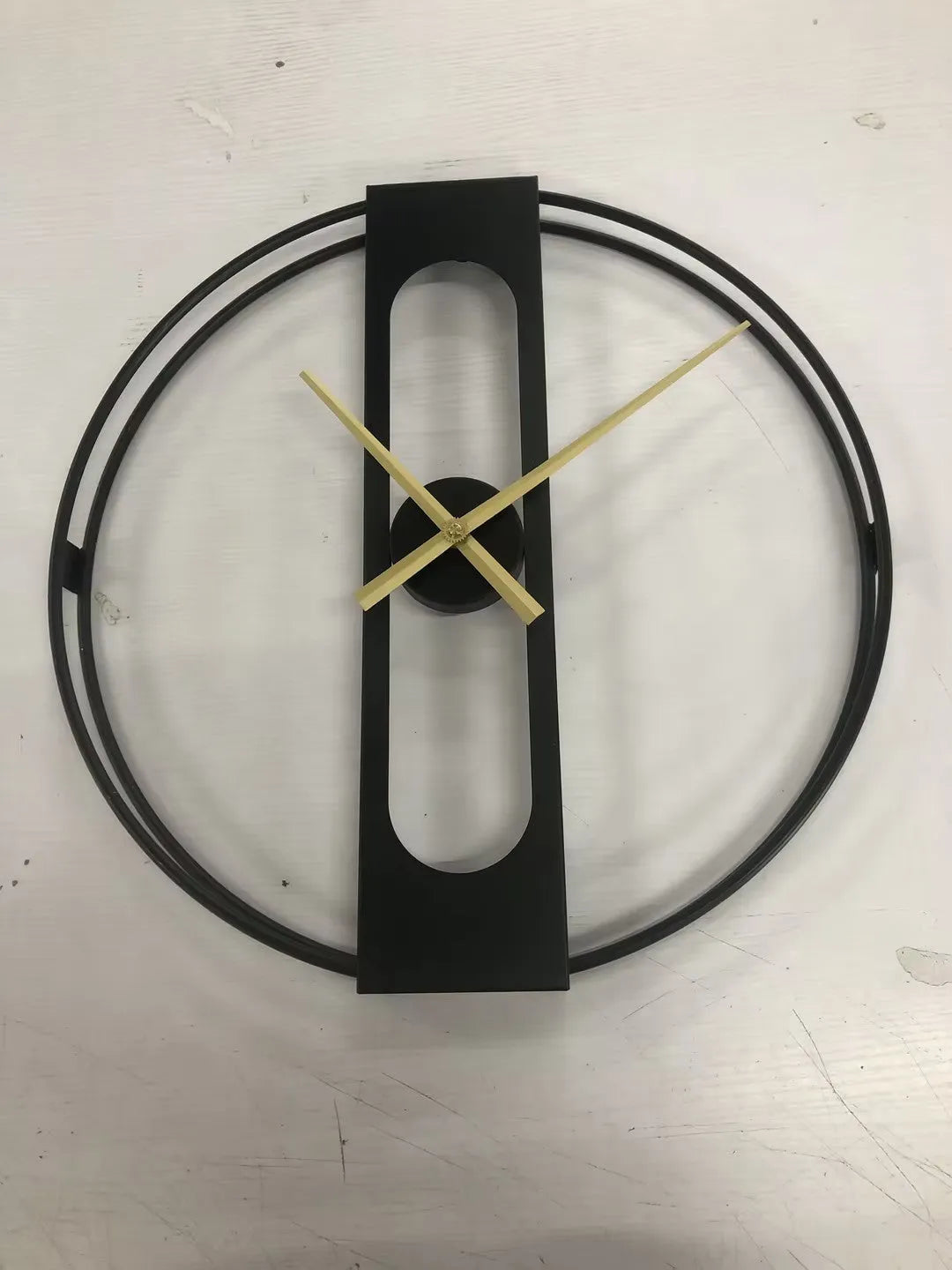 Round metal wall clock with 50cm diameter in black or gold colour on a white wall.