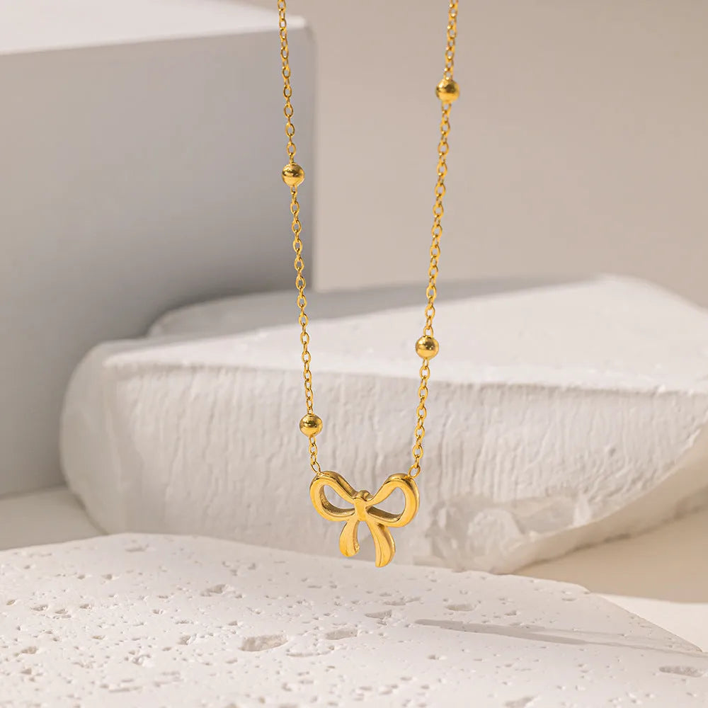 Gold electroplated women's bow necklace with cross chain design on white background