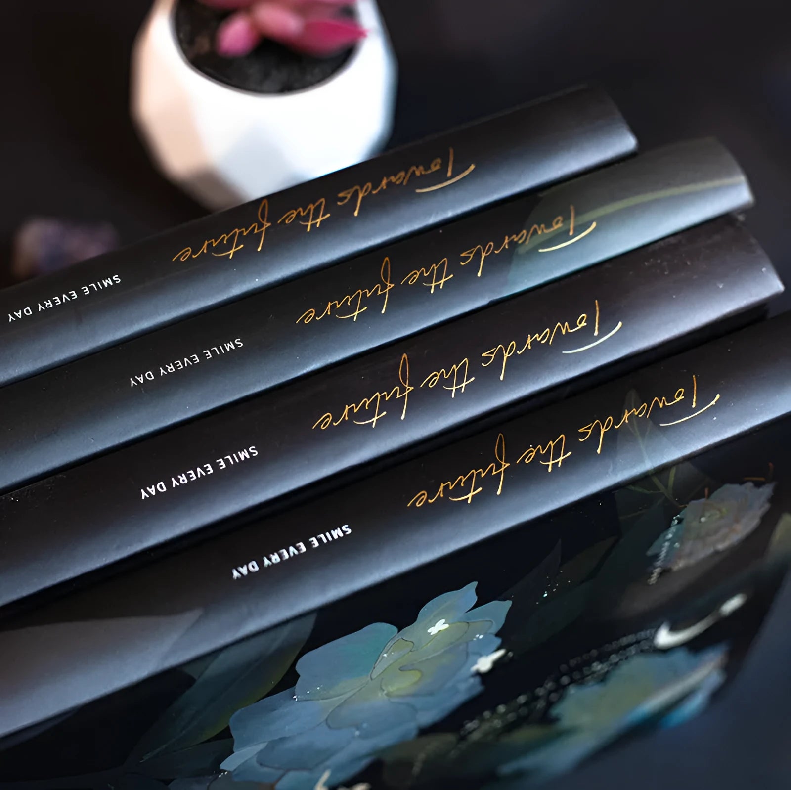 A5 notebook with luminous cover open to show internal colour illustrations, in Deep Blue, Gold, Light Blue, and Purple options