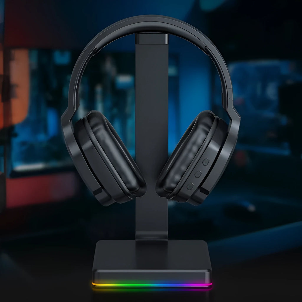 Luminous black wireless gaming headphones with head-mounted design on a desk with included 3.5mm cable and dust bag.