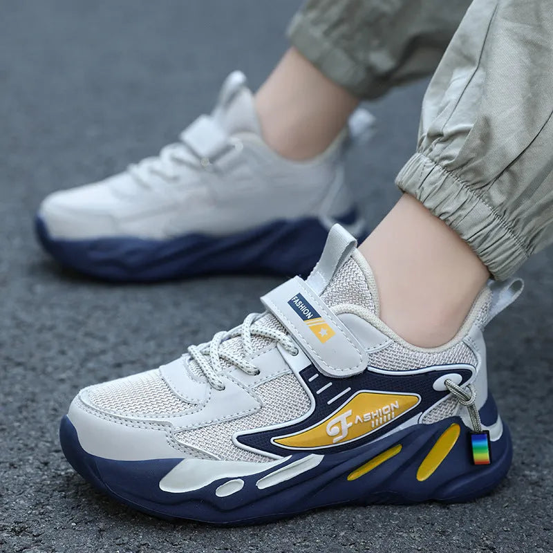 Boys sports running shoes in dark blue with a mesh upper and Velcro strap, shown on a hard ground surface.