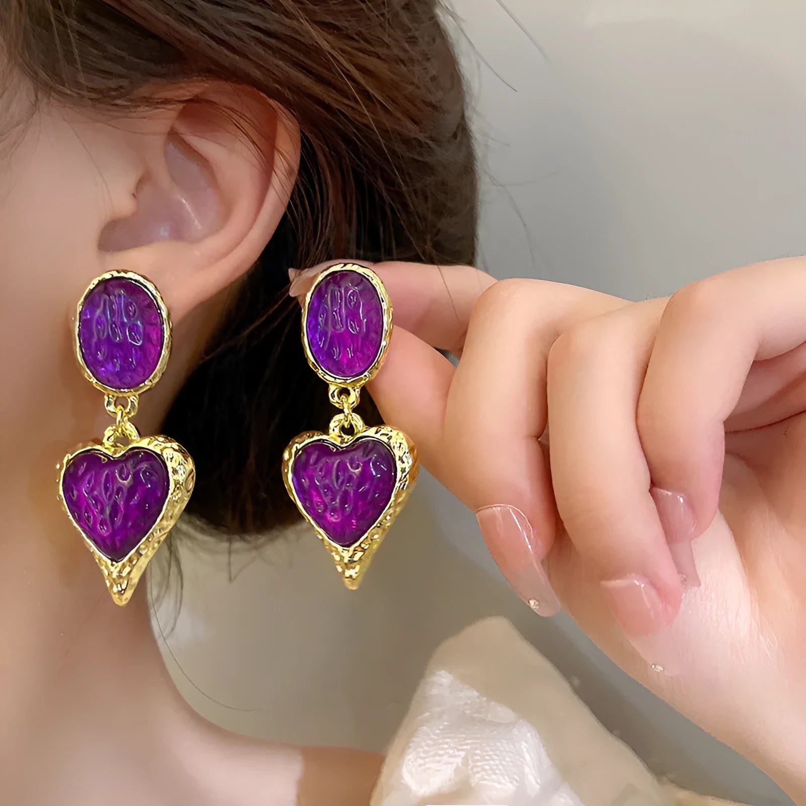 Close-up of a pair of textured needle-pleated oval heart stud earrings in an alloy metal, showing colour options.